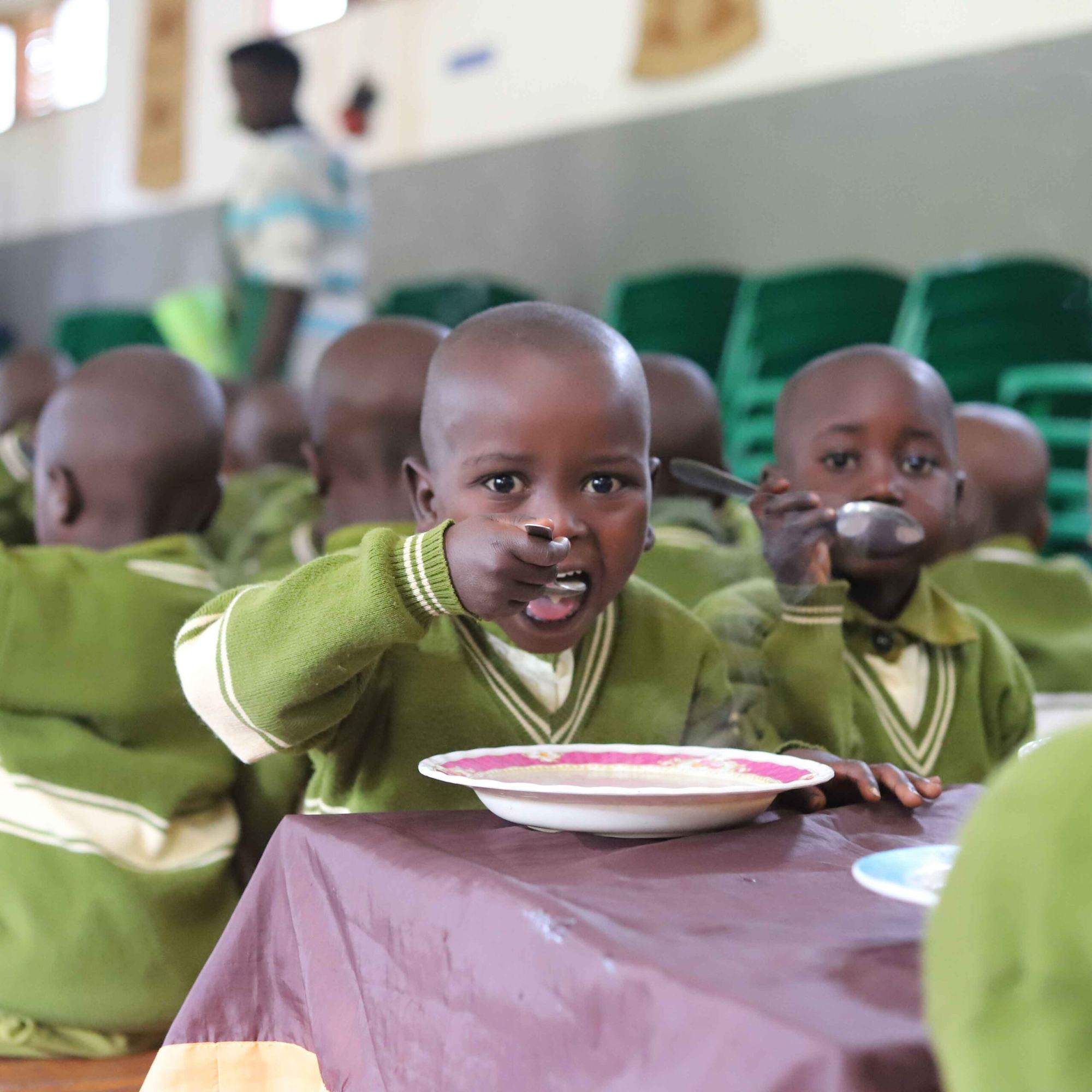Children in green school uniforms drinking fortified porridge at a table in Burundi